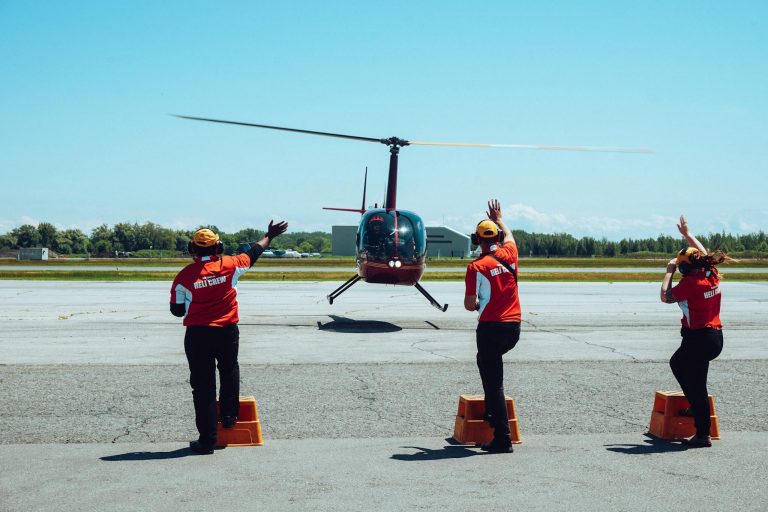 Back view of anonymous ground crews in uniforms and headsets meeting passenger helicopter on airfield after flight against cloudless blue sky